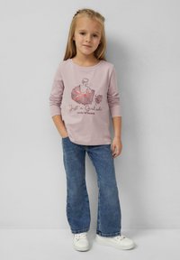 Jasnoróżowa koszula z długim rękawem z grafiką tancerza z błyszczącymi akcentami, zestawiona z niebieskimi dżinsami z rozszerzanymi nogawkami i białymi trampkami.