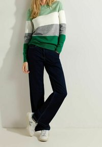 Suéter a rayas en verde, blanco y gris; combinado con jeans oscuros y zapatillas blancas. El suéter tiene puños y dobladillo acanalados.