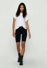 Zwarte biker shorts, wit t-shirt en zwarte enkellaarzen. Glad materiaal, losse pasvorm voor de bovenkant, shorts tot halverwege de dij. Eenvoudig ontwerp.
