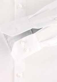 Primo piano di polsini di camicia bianca con polsini a barile abbottonati e bottoni visibili su tessuto liscio.