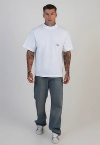 Biała bawełniana koszulka z okrągłym dekoltem i krótkimi rękawami, zestawiona z jasnoniebieskimi jeansami o prostych nogawkach i białymi sneakersami. Proste haftowane logo.