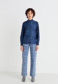 Camicia a maniche lunghe con bottoni in motivo floreale blu, abbinata a jeans a gamba larga blu chiaro con dettagli in argento. 