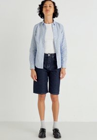 Maglietta azzurra a righe con bottoni, t-shirt bianca, pantaloni corti in denim scuro, calzini grigi, scarpe nere. Design semplice con vestibilità rilassata e stili classici.