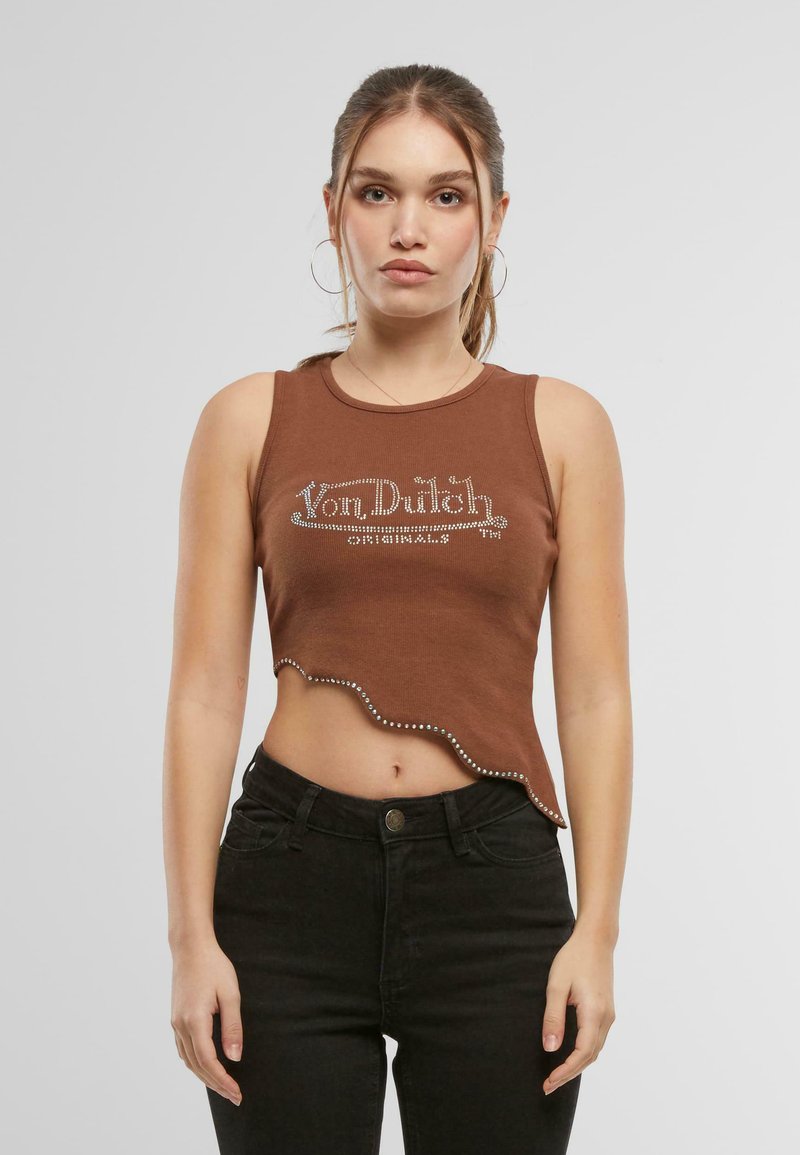 Brun kortärmad top med vågig fåll och nitar som visar "Von Dutch"-logotypen. Klädd med svarta högmidjade byxor.