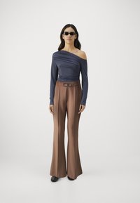 Námornícky off-shoulder top s textúrovaným drapovaním, spárovaný s vysokými hnedými flared nohavicami so zaväzovaním a prackou. Čierne elegantné topánky.