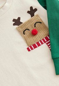 Cremefarbenes Sweatshirt mit einem tanfarbenen Rentierge Gesicht, braunen Geweihen, einer roten Pompon-Nase und einem gestreiften Schal in Rot und Weiß.