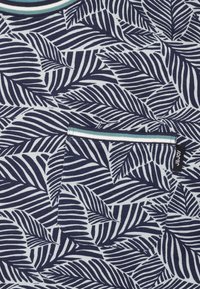 Marineblauwe en witte gestreepte stof met gestileerde bladeren. Inclusief een met teal accenten uitgevoerd zakje en een contrasterende ribbelneklijn.