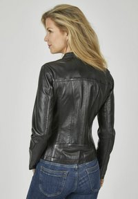 Schwarze Lederjacke mit tailliertem Design, Nahtdetails und hohem Kragen. Über blauen Denim-Jeans getragen, die eine glatte Textur zeigen.