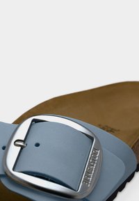 Ανοιχτό μπλε, απαλό δερμάτινο σανδάλι με φαρδιά λουρίδα και ασημένια ορθογώνια αγκράφα. Καφέ σουέντ εσωτερικό πέλμα και μαύρη λαστιχένια σόλα.