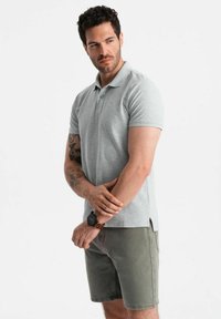 Grå polo med kort ärm, mjuk textur och knäppt krage, kombinerad med ljus olivgröna shorts, som visar en subtil logotypdetalj.