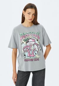 Camiseta de algodón gris de manga corta con un gráfico colorido de champiñones y el texto "Vida Positiva y Groovy" en el frontal.