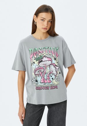 Camiseta de algodón gris de manga corta con un gráfico colorido de champiñones y el texto "Vida Positiva y Groovy" en el frontal.