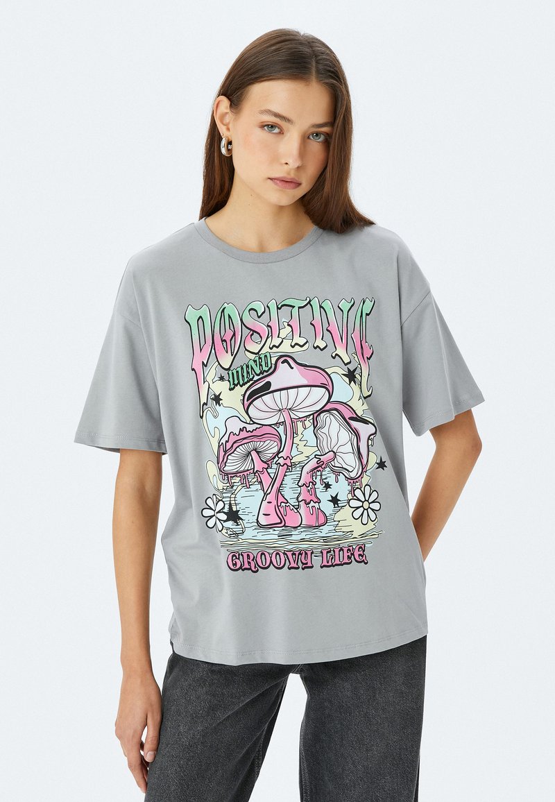 Grijze katoenen t-shirt met korte mouwen, voorzien van een kleurrafische afbeelding van paddenstoelen en de tekst "Positieve Groovy Leven" op de voorkant.