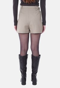 Pantaloni tailored beige con una consistenza liscia e un taglio dritto, abbinati a collant neri trasparenti e stivali neri fino al ginocchio.