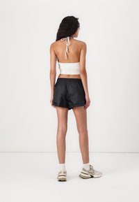 Black lightweight shorts with an elastic waistband, paired with a white cropped halter top. Shoes are beige with grey accents.
