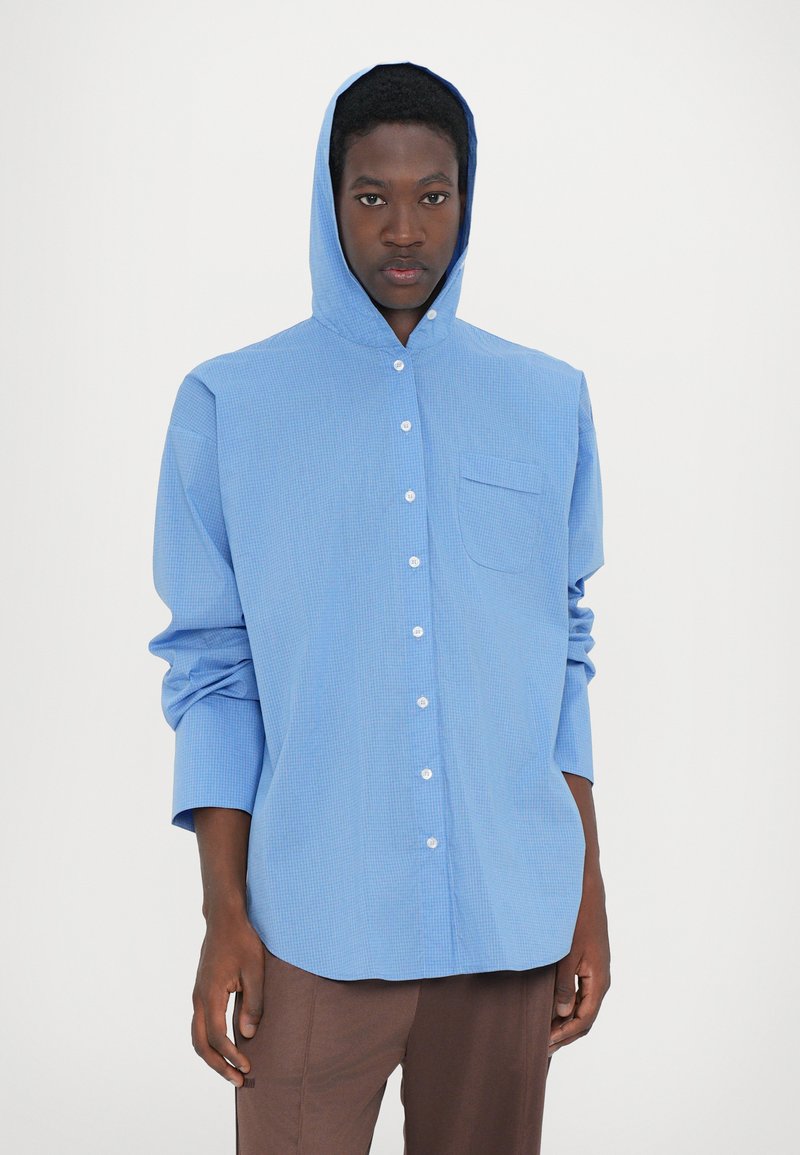 Camisa a cuadros azul con capucha, cierre frontal con botones, un bolsillo en el pecho y mangas largas, fabricada con una tela ligera.