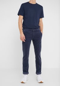 Laivastonsininen puuvillainen t-paita yhdistettynä tummansinisiin corduroy-housuihin, jotka on kääräisty lahkeista. Valkoiset urheilukengät täydentävät asun.