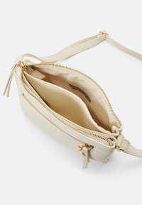 Torebka na ramię z jasnobeżowej skóry z złotymi zamkami błyskawicznymi, o kompaktowym kształcie i dwoma kieszeniami wewnętrznymi do uporządkowanego przechowywania.