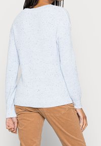 Ljusblå stickad tröja med en struktur av små prickar. Har långa ärmar och rundad halsringning, avslut vid höfterna.