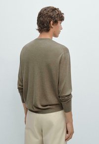 Maglione leggero marrone con maniche lunghe, scollo rotondo e una sottile texture, indossato su pantaloni di colore chiaro. La vista posteriore mostra una vestibilità comoda.