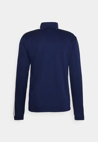 Námořnická modrá bunda s dlouhými rukávy a vysokým límcem, s bílými pruhy na ramenou. Hladká textura, ležérní design.