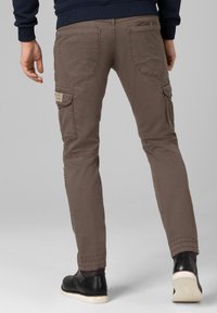 Brown cargo pants with four pockets, tapered design, and elastic cuffs. Made of durable fabric with visible stitching and subtle branding details.