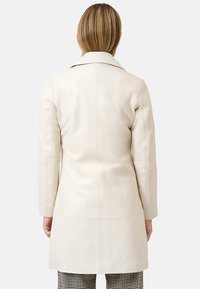 Beige leren jas met een reverskraag, op maat gemaakte pasvorm en een rechte silhouet, voorzien van stikseldetails, gedragen over houndstooth broek.