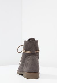 Botín de ante gris de tobillo con puntera redonda, textura suave y un detalle de cordones marrón claro que envuelve el tobillo.