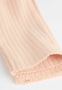 Ribbet, let materiale i blød ferskenfarve. Har en bølget kant og subtil tekstur, hvilket antyder et tætsiddende design.