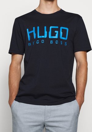 Granatowa koszulka z miękkiej bawełny, z wyraźnym, jasnoniebieskim napisem "HUGO" oraz logo "hugo boss" w nowoczesnej czcionce. Krótkie rękawy, okrągły dekolt.