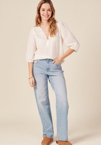 Weiße Blumenbluse mit Dreiviertelärmeln, Knopfleiste, kombiniert mit hellblauen, geraden Jeans und braunen Stiefeletten.