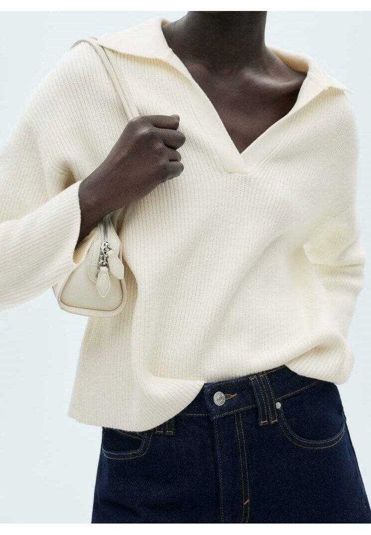 Cremefarbenes, geripptes Strickpullover mit V-Ausschnitt und weitem Kragen, kombiniert mit dunklem Denim-Jeans und einer kleinen hellen Handtasche.