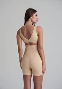 Completo sportivo beige composto da un reggiseno seamless con spalline larghe e un pantalone a vita alta. Tessuto liscio e elasticizzato con un design aderente.