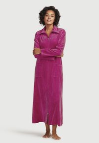 Lång, dragkedjeslupen kappa i livlig fuchsia. Tillverkad av mjukt, texturerat tyg med två stora frontfickor och en krage.