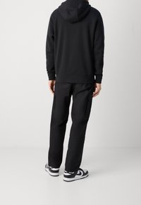 Sudadera negra con bolsillo canguro, combinada con pantalones cargo negros a juego que tienen bolsillos laterales y zapatillas negras y blancas.