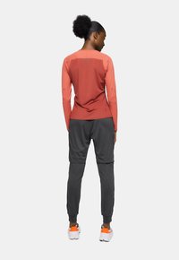 T-shirt de sport à manches longues couleur corail avec des panneaux texturés, associé à un jogging gris foncé et des chaussures blanches avec des accents orange.