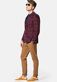 Bordowy dwurzędowy blezer w kratę, niebieska koszulka z okrągłym dekoltem, beżowe slim-fit spodnie i żółte sportowe buty. Okulary przeciwsłoneczne dopełniają stylizację. Dopasowana pozę.