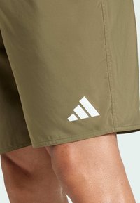 Olivově zelené šortky vyrobené z lehkého materiálu; na spodní straně se nachází bílé logo se třemi pruhy; hladká textura a rovný střih.