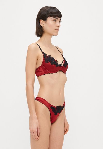 Punane satiinist rinnahoidja ja stringkomplekt musta pitsi äärise ning lilledega aktsentidega; sisaldab reguleeritavaid rihmasid ja dekoratiivõmblusi servades.