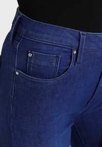 Mörkblå denimjeans med en slät textur, som har framfickor, silverdetaljer och en hög midja.
