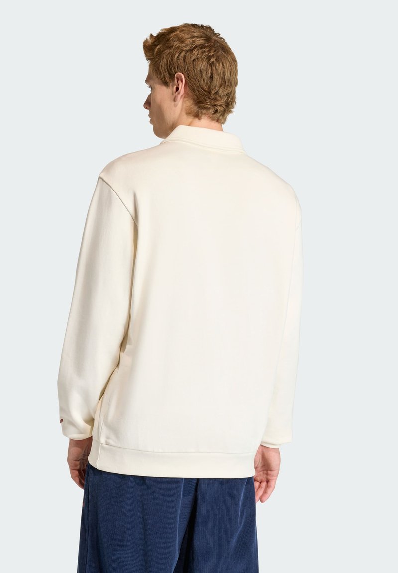 Sweatshirt beige clair avec une coupe décontractée, manches longues et ourlet côtelé, présentant des coutures minimales et une texture lisse.