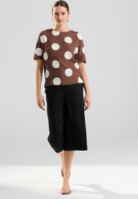 Haut à pois marron avec des cercles crème, manches courtes, col rond, associé à un pantalon large noir et des sandales à lanières simples.