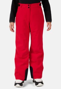 Pantaloni da sci impermeabili rossi con vestibilità ampia, dotati di chiusura a bottone, due tasche frontali e dettagli neri all'orlo.
