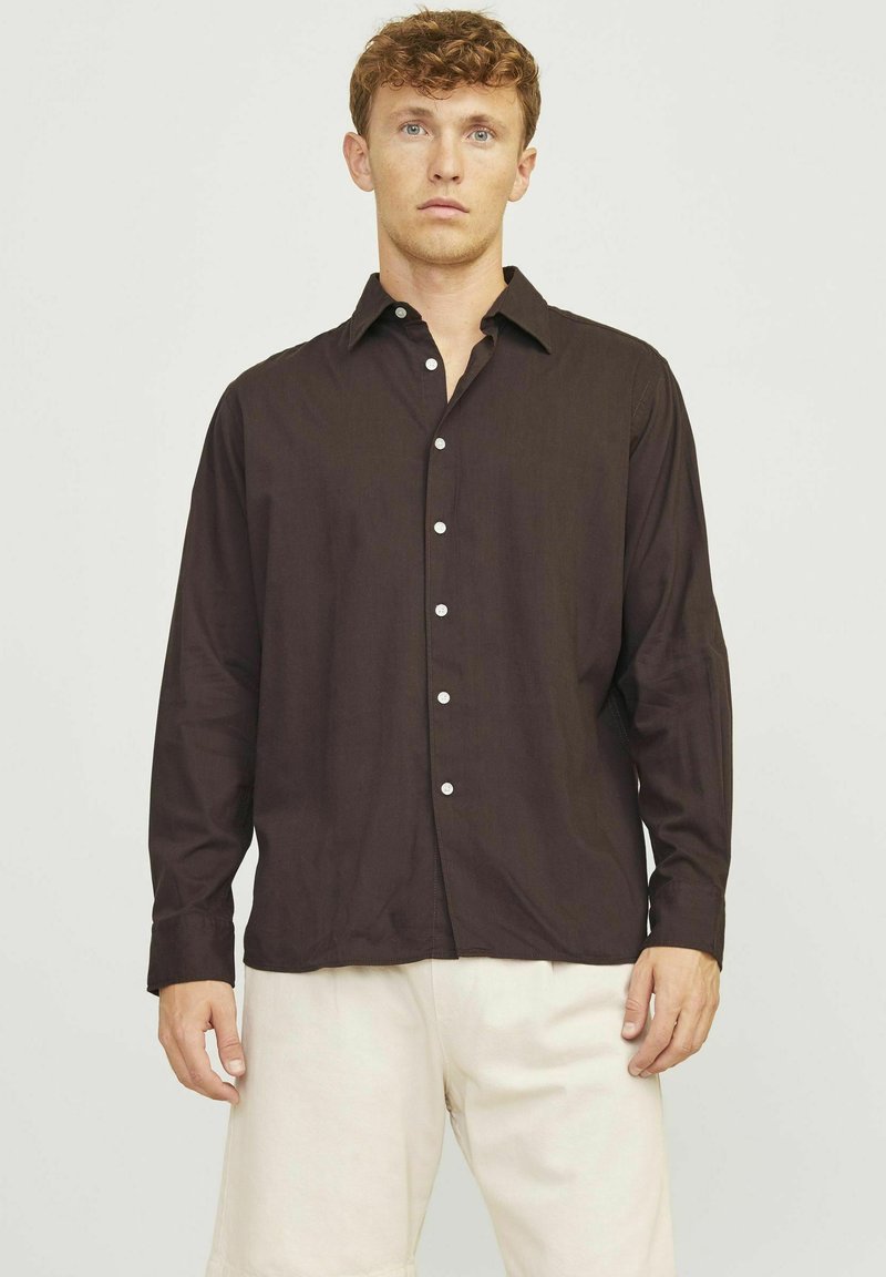 Dunkelbraunes Hemd mit Knöpfen, Kragen, langen Ärmeln und weißen Knöpfen. Kombiniert mit hellbeigen Shorts. Einfaches Design und glatte Textur.