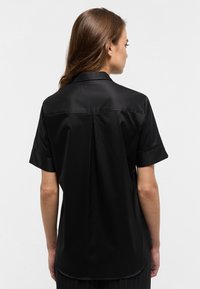 Maglietta nera a maniche corte realizzata in tessuto morbido, con colletto classico, piega sul retro e vestibilità rilassata, con orlo curvo.