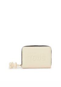 Cartera de cuero crema con cierre de cremallera, que presenta un logo embossado en la parte delantera y un charm decorativo en forma de pompom adjunto. Forma rectangular compacta.