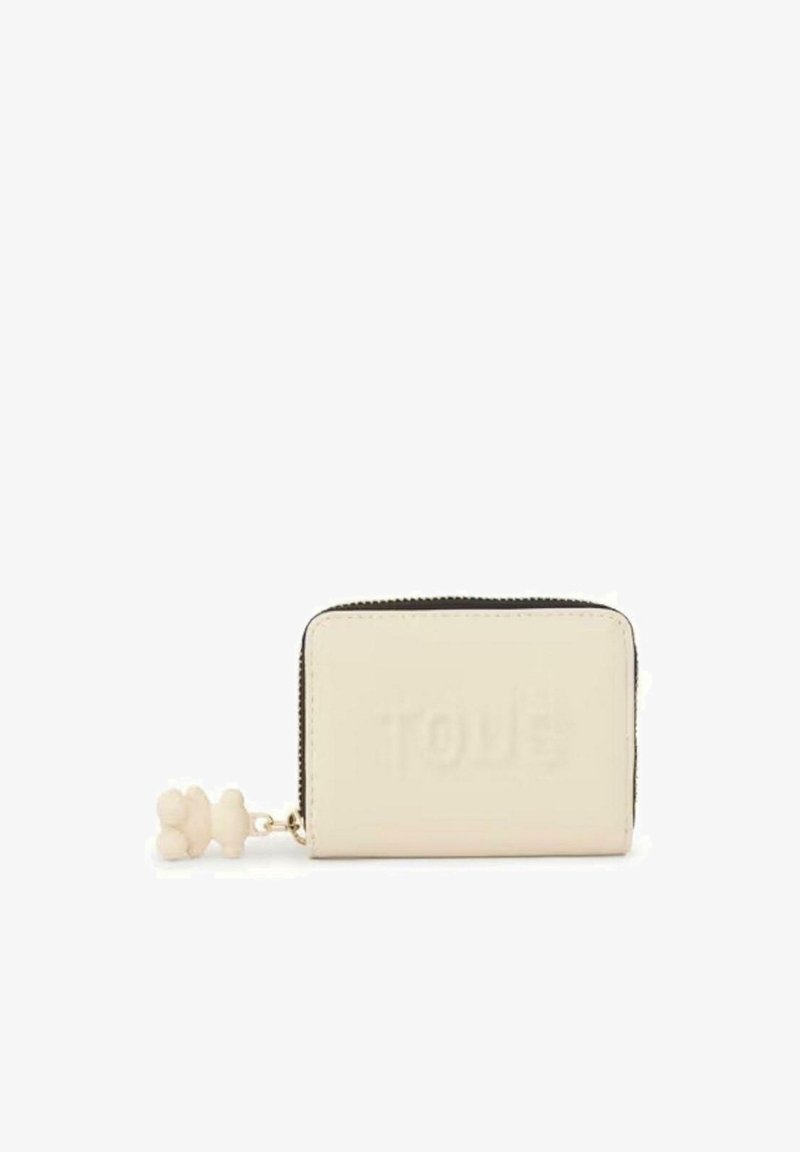 Cartera de cuero crema con cierre de cremallera, que presenta un logo embossado en la parte delantera y un charm decorativo en forma de pompom adjunto. Forma rectangular compacta.