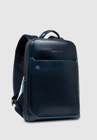 Mochila de cuero azul marino con un diseño elegante, cierre con cremallera, respaldo acolchado y acentos en azul claro que contrastan. Cuenta con un logo en la parte frontal.