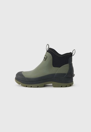 Kotníková nepromokavá bota v olivově zelené a černé barvě s pásky pro snadné nazouvání, texturovanou podrážkou a logem Barbour na boku, zobrazená z vnější strany.