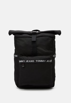Czarny plecak z rolowanym zamknięciem, przednią kieszenią na zamek i paskami z logo „Tommy Jeans” na kieszeni i bocznych częściach na jednolitym tle.